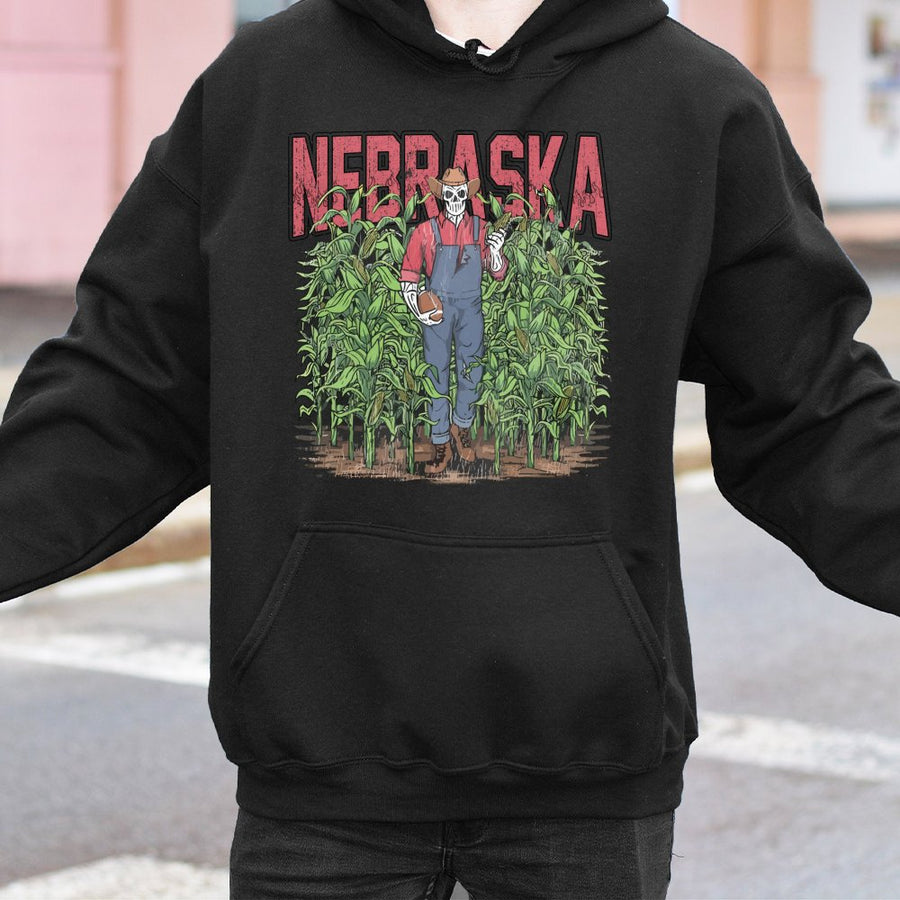 Nebraska With A Skeleton Dressed As A Farmer In Overalls Holding A Football And An Ear Of Corn While Standing In A Cornfield Hoodie