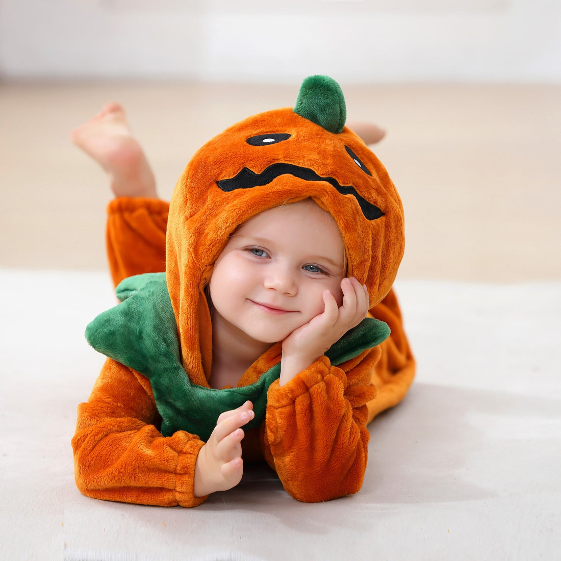 Child lying down in the pumpkin romper, hood up