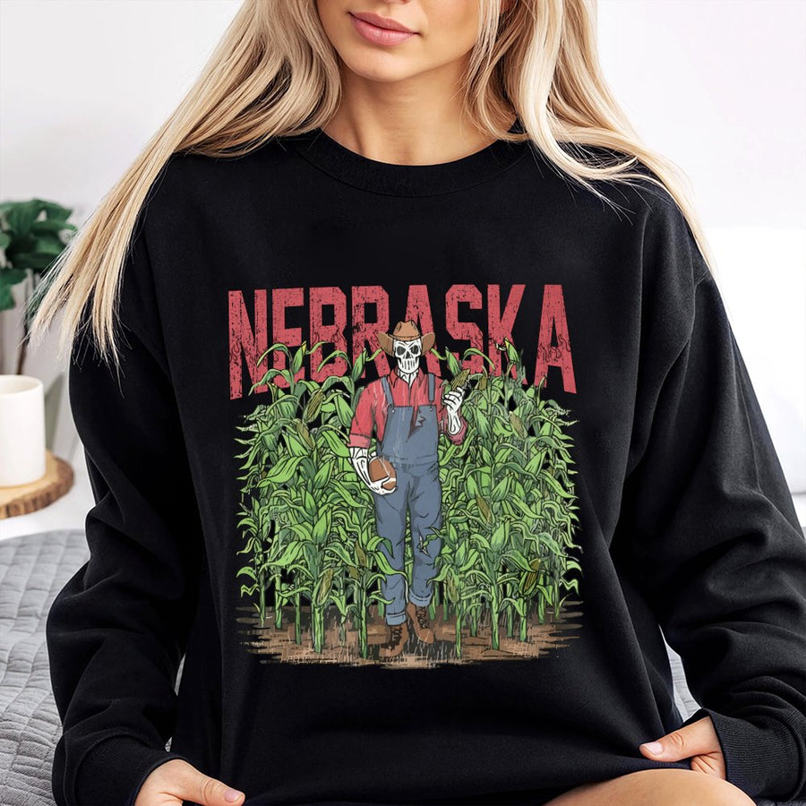 Nebraska With A Skeleton Dressed As A Farmer In Overalls Holding A Football And An Ear Of Corn While Standing In A Cornfield Sweatshirt