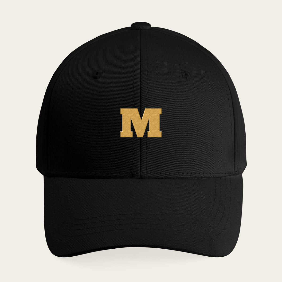A black cap with a single large initial stitched in gold thread