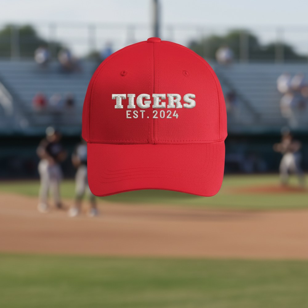 Red cap embroidered TIGERS EST. 2024 on a ball field at golden hour