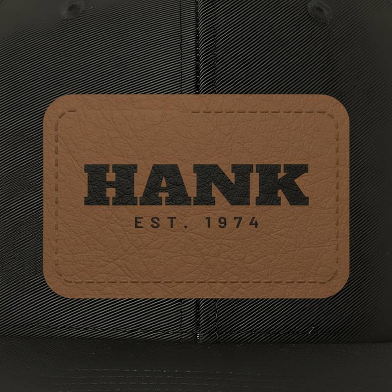 Close-up of a black cap with a leather patch engraved HANK, EST. 1974